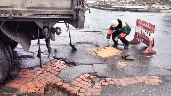 Ямы на асфальтовой дороге, засыпанные щебнем и закрытые кирпичом